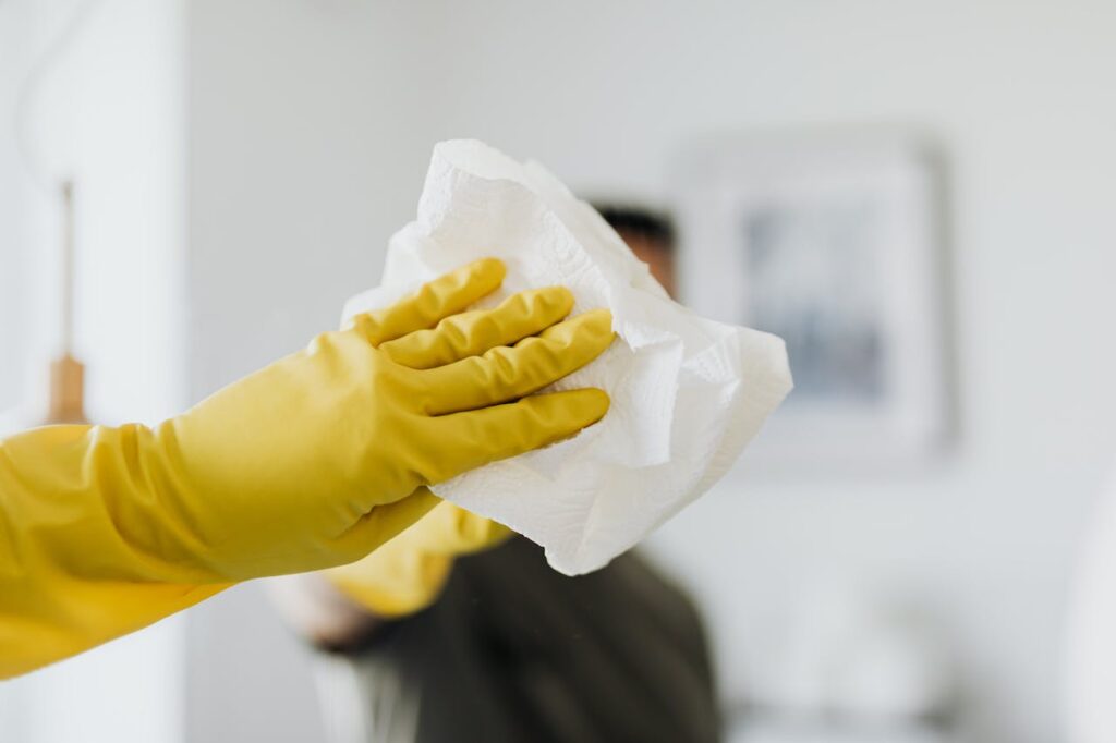 pexels photo 4239127 Close-up of a yellow-gloved hand cleaning a mirror with a cloth indoors.